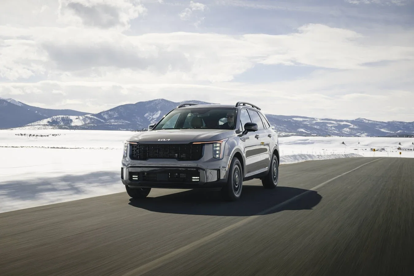 A Kia SUV on a road with snowy mountains behind it.