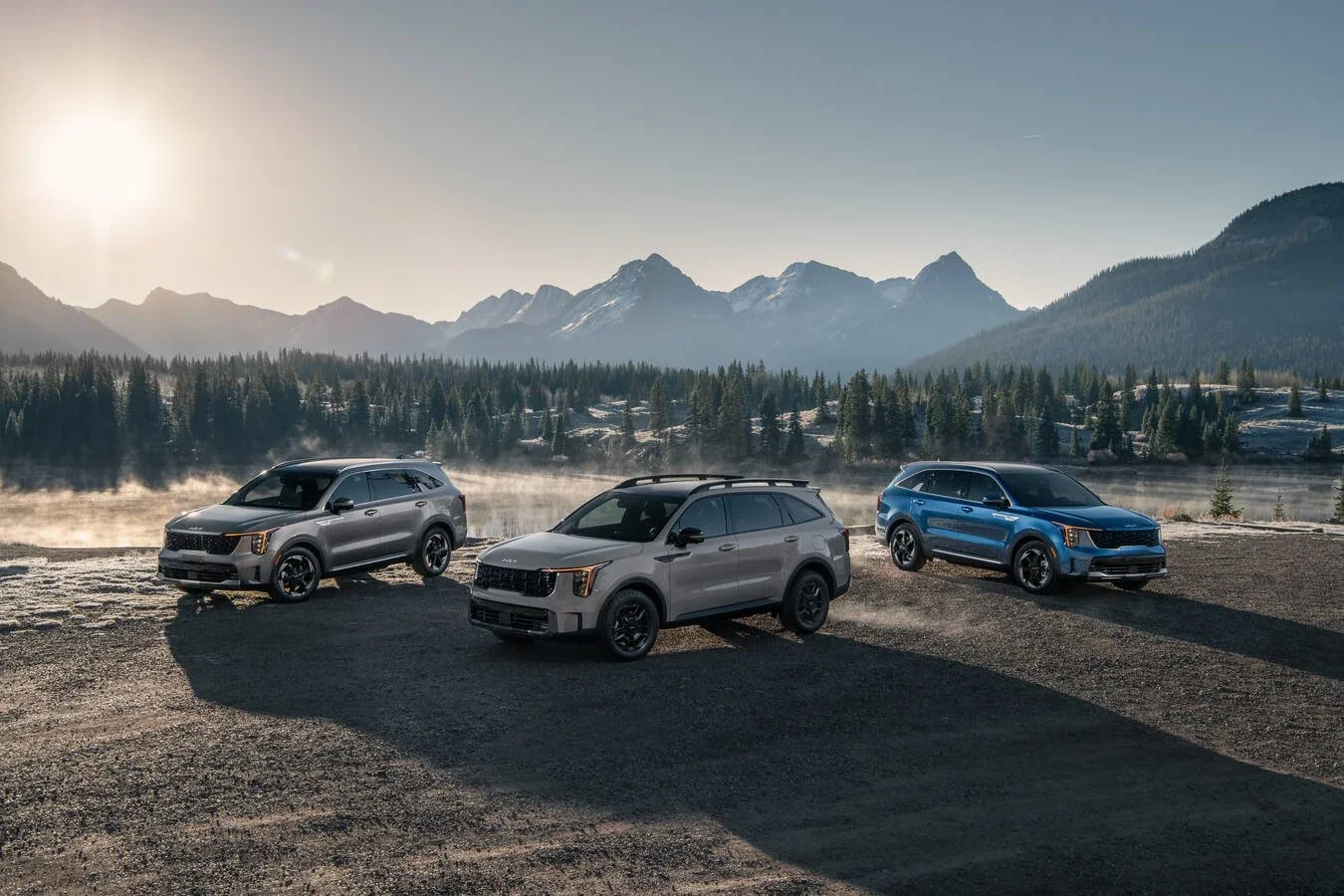 Three Kia SUVs parked below the mountains at dusk.