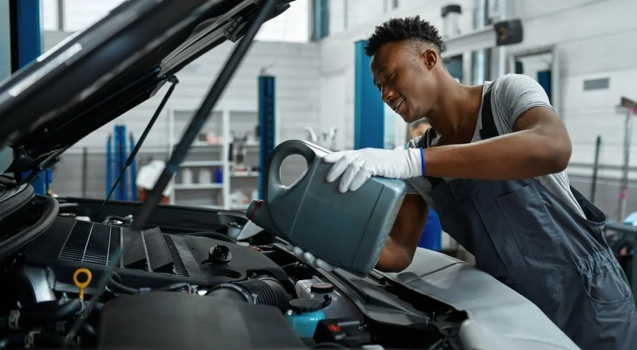 A technician pouring fresh oil into the engine of a Kia in a service bay.