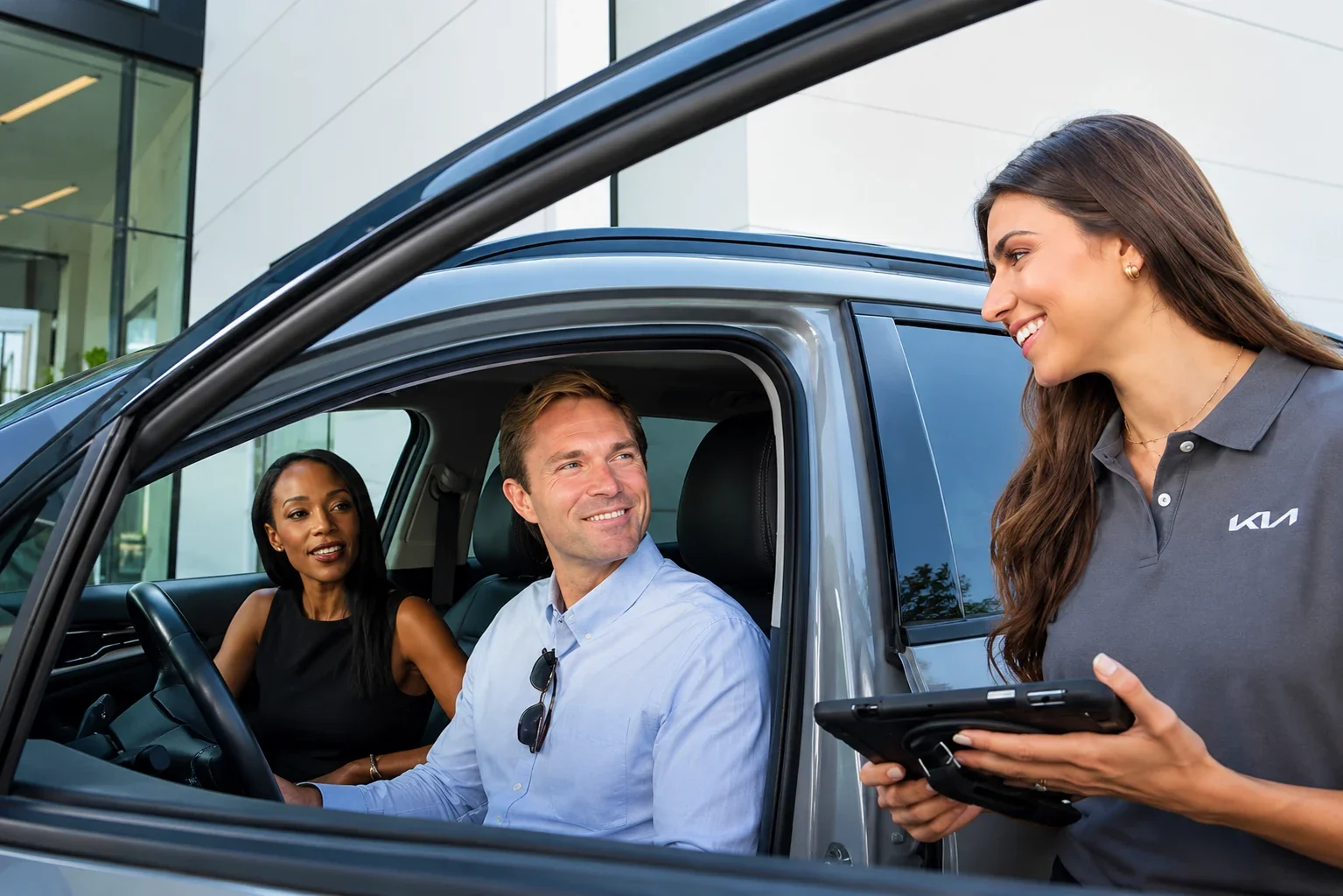 A Kia service advisor with a tablet greeting a couple in their car at the service drive.