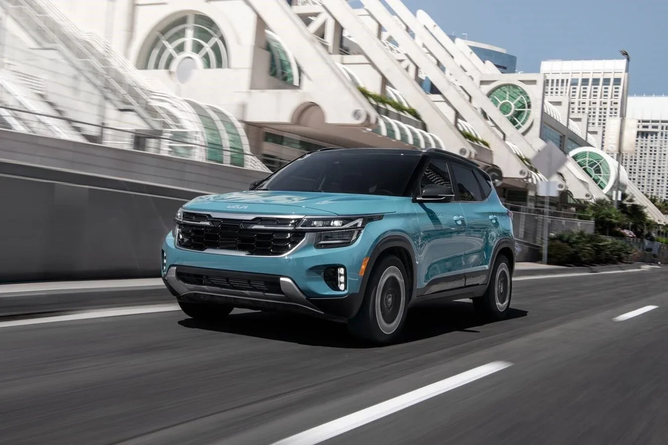 A teal Kia Seltos driving through the city.