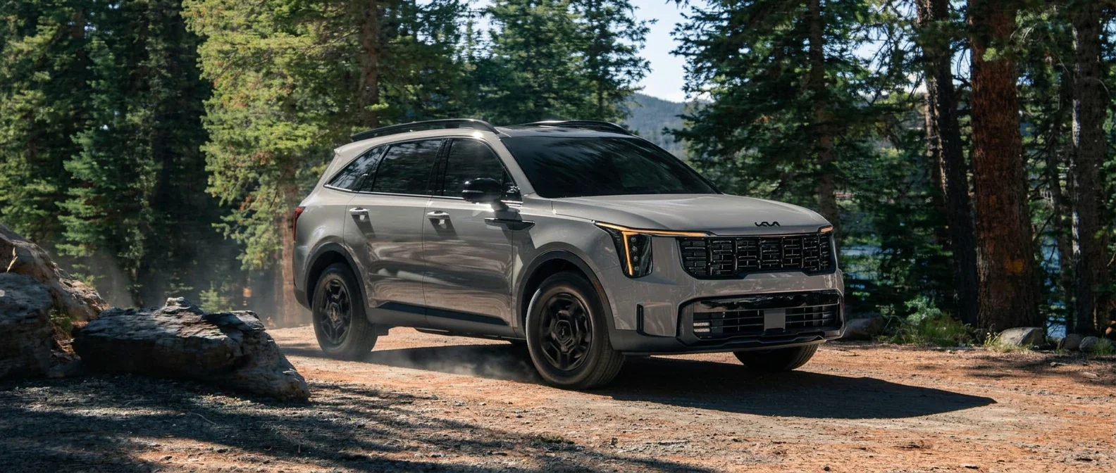 A Kia Sorento parked on a dirt clearing in a pine forest.