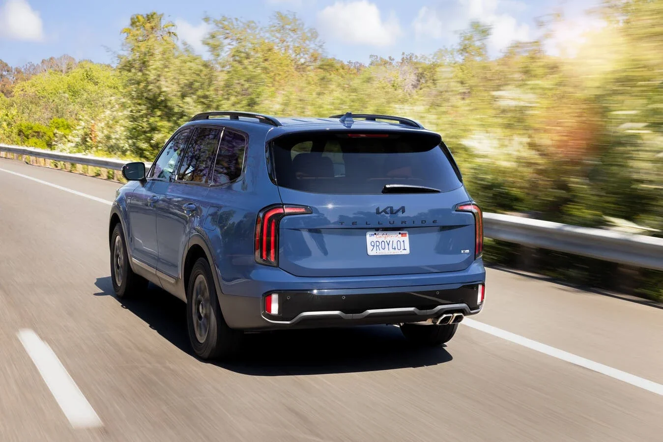 A blue Kia Telluride on the highway, seen from behind.