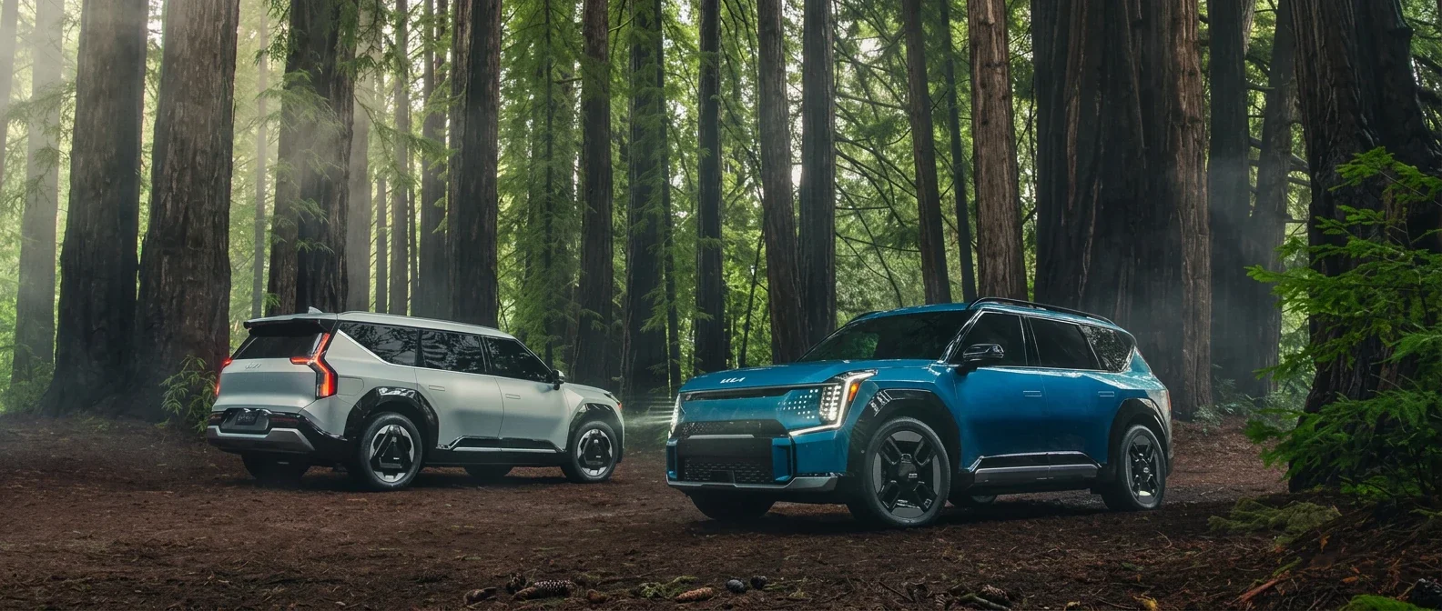 Two Kia EV9s, one white and one blue, parked in a redwood forest.