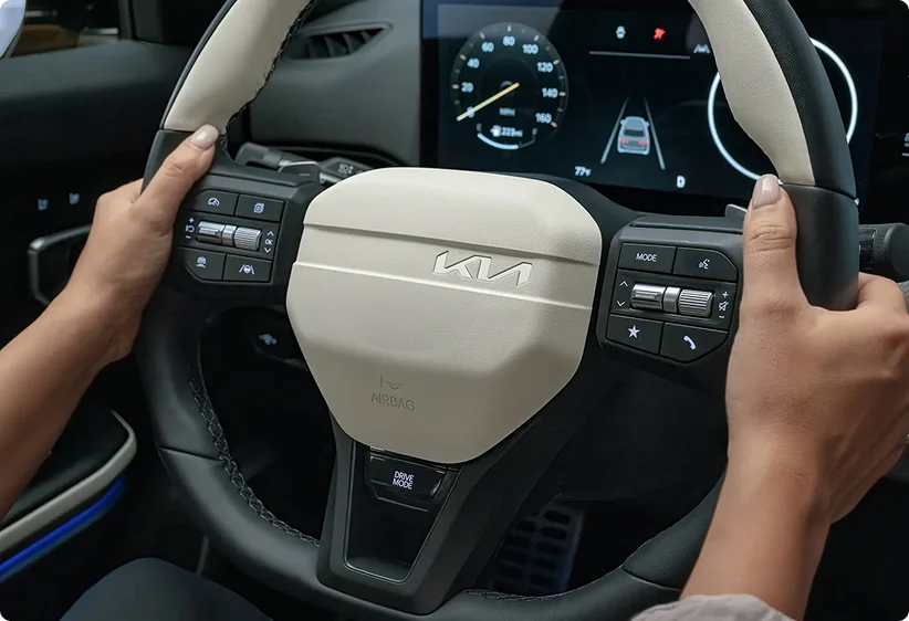 Driver's hands on the 2026 Kia K4 three-spoke sport steering wheel with a light beige airbag cover and mounted controls