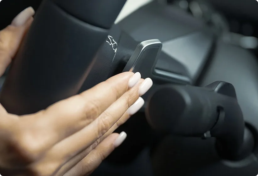 Driver's hand reaching for the steering wheel-mounted paddle shifter behind the 2026 Kia K4 steering wheel