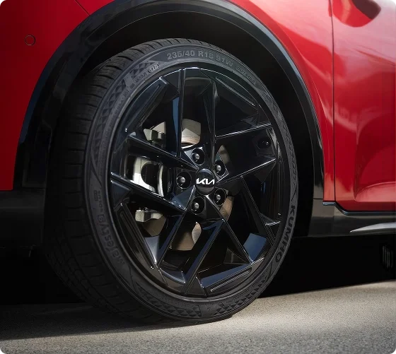 Close-up of a black machined alloy wheel with a Kia center cap on a red 2026 Kia K4