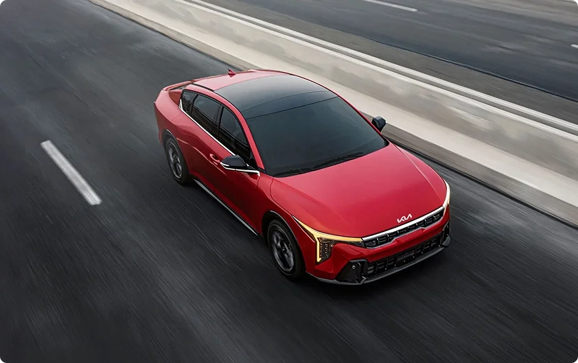 Aerial view of a red 2026 Kia K4 on a highway showing the glass of its ultra-wide sunroof