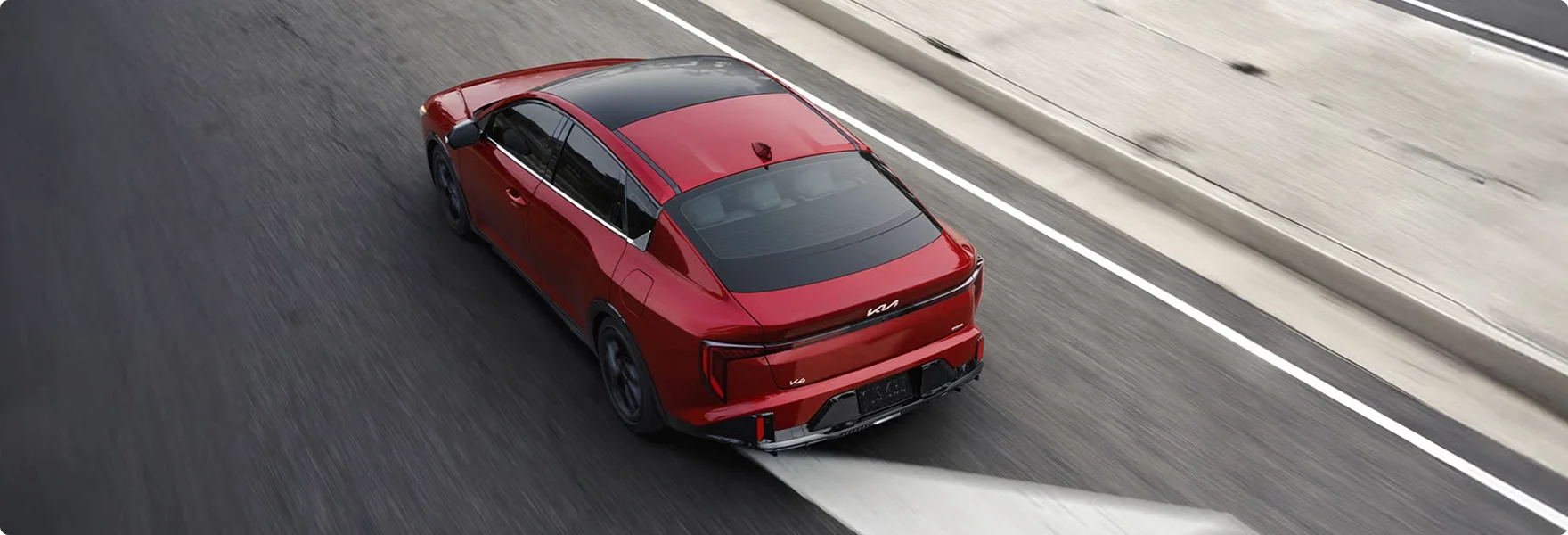 Red 2026 Kia K4 driving on a multi-lane highway seen from a high rear angle