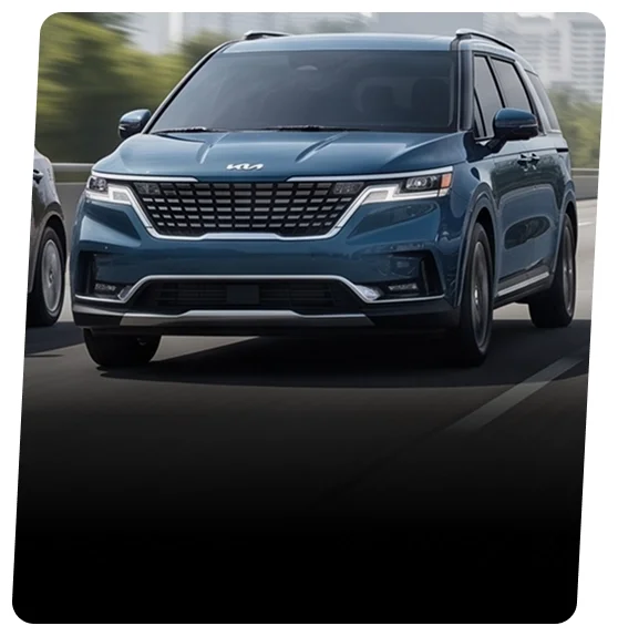 Blue Kia Carnival minivan shown head-on with a city skyline blurred behind it