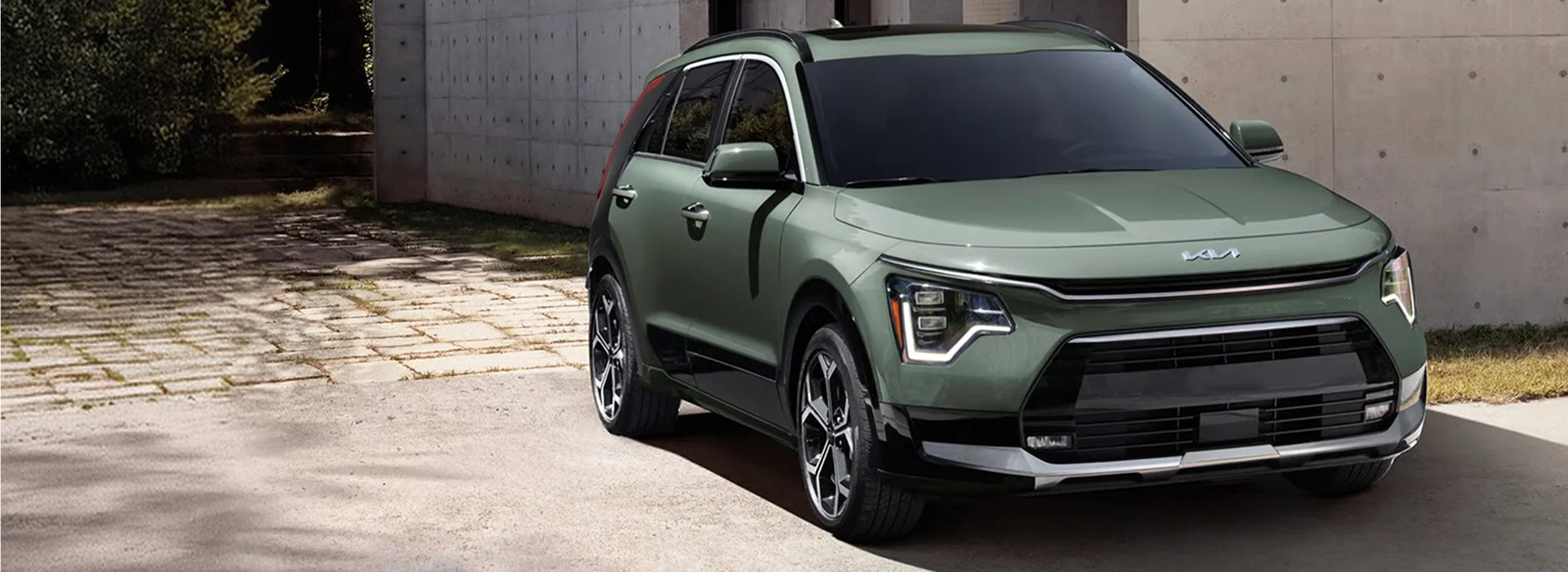 Sage green 2026 Kia Niro Hybrid parked on a paved drive beside a poured-concrete wall