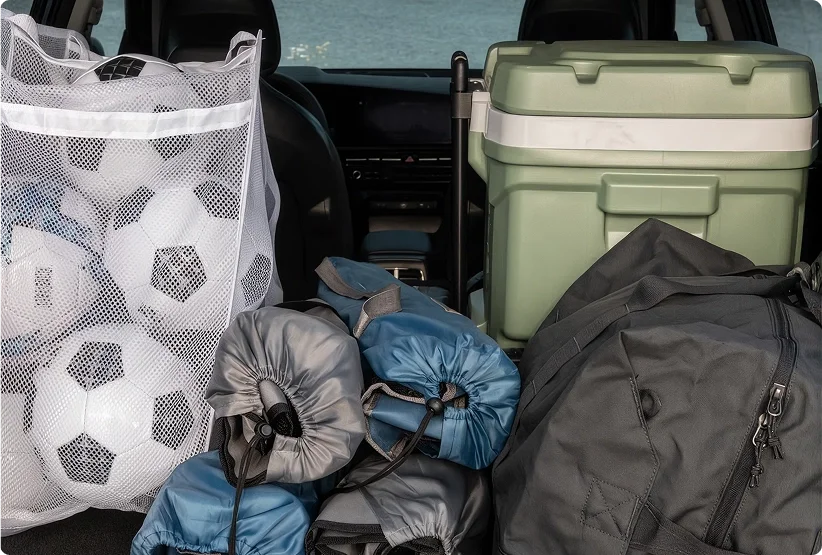 2026 Kia Niro Hybrid cargo area packed with a mesh bag of soccer balls, sleeping bags, a green cooler and a duffel bag