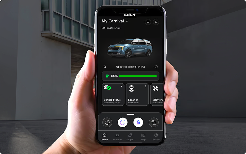 Hand holding a smartphone showing the Kia Connect app with a Carnival MPV on screen