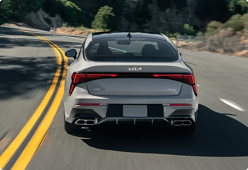 Kia K5 seen from behind taking a curve on a mountain road