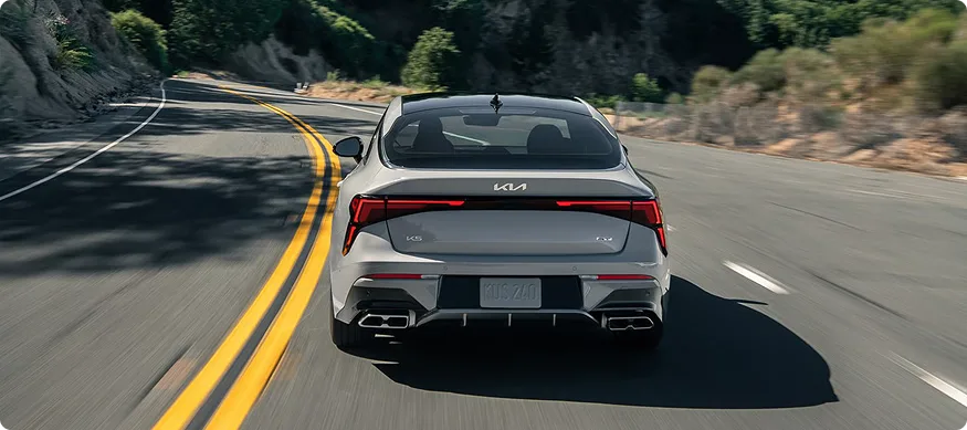 Kia K5 seen from behind on a winding mountain road