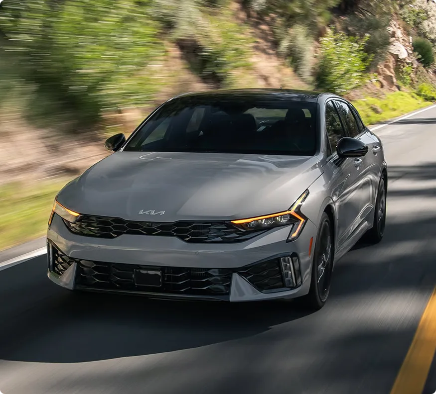 Grey Kia K5 driving on a mountain road, front three-quarter view