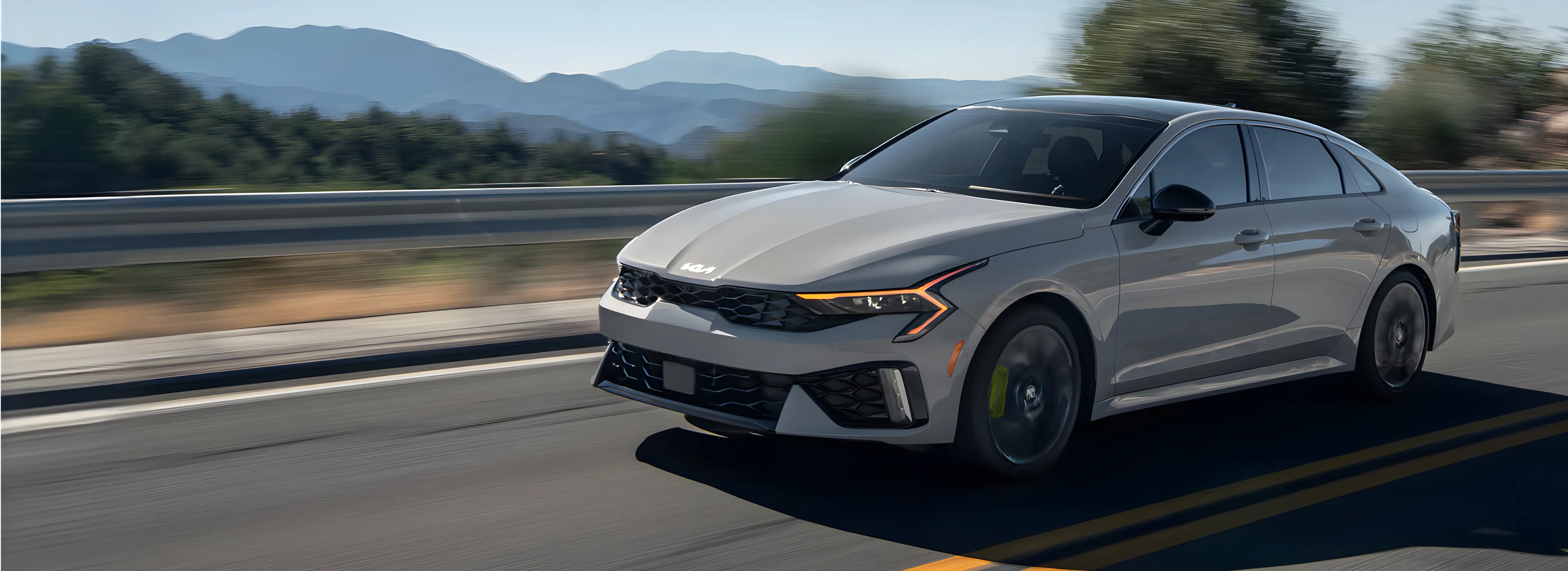 Grey 2027 Kia K5 driving on a mountain highway