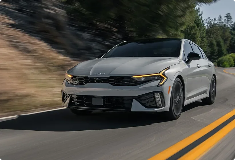Kia K5 cornering on a winding tree-lined road