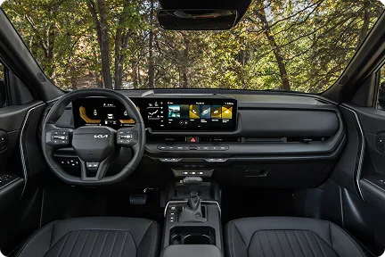 Seltos cockpit with the curved dual displays lit and forest visible through the windshield