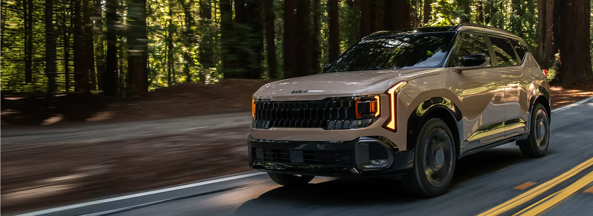 Bronze 2027 Kia Seltos driving on a road winding through tall redwood trees