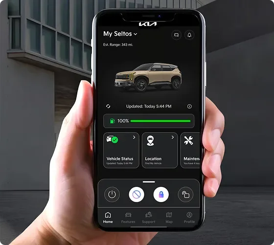 Hand holding a smartphone running the Kia app, showing My Seltos and its estimated range