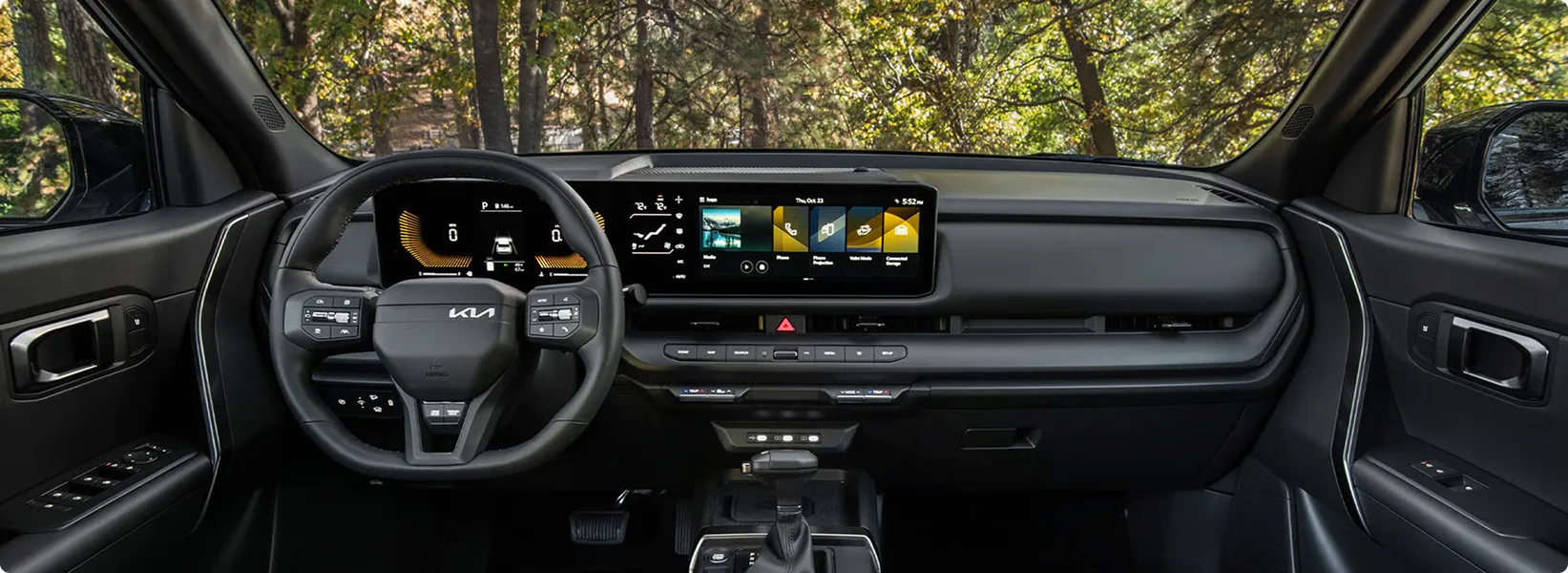 Seltos cockpit with the curved dual displays lit and forest visible through the windshield