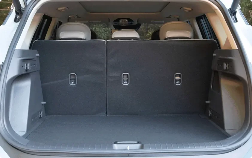 Open Seltos cargo area with the rear seats folded flat, forest visible behind the vehicle