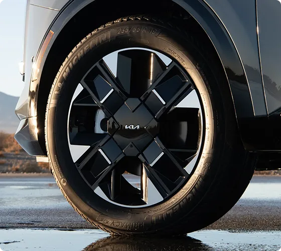 Close-up of a black Sportage Hybrid alloy wheel with the Kia centre cap, on wet ground