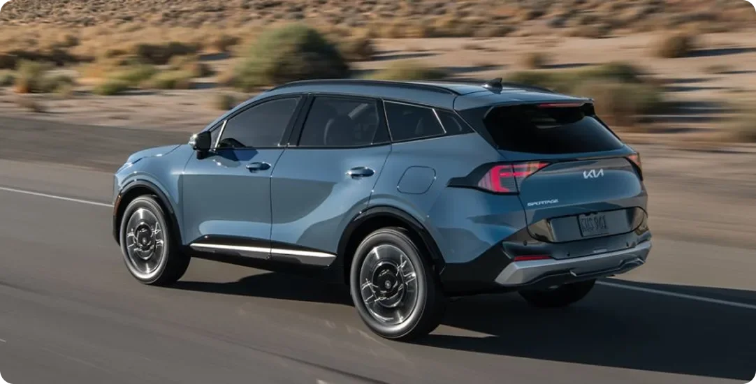 Blue 2027 Kia Sportage Hybrid driving away on a desert highway, rear three-quarter view