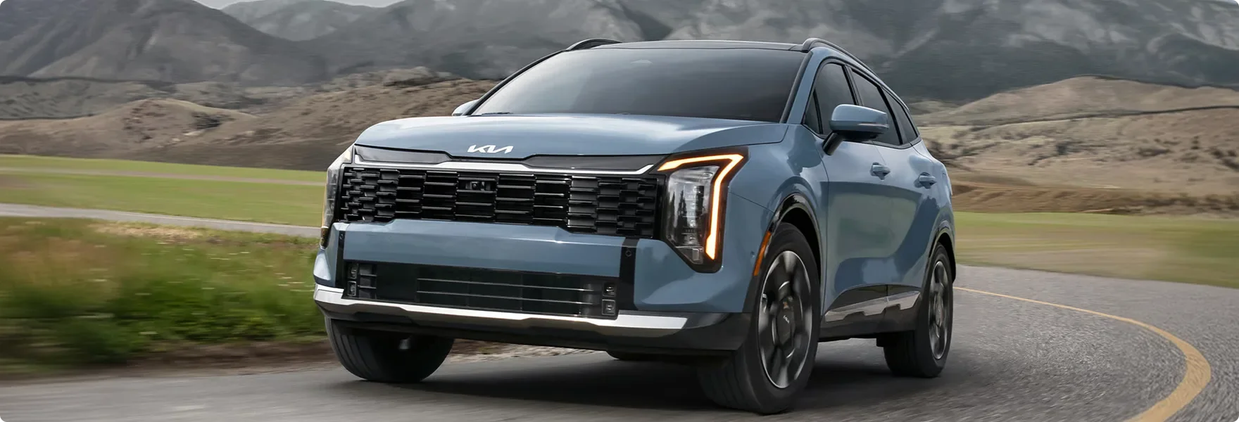 Light blue 2027 Kia Sportage Hybrid driving on a country road toward the camera, with hills behind