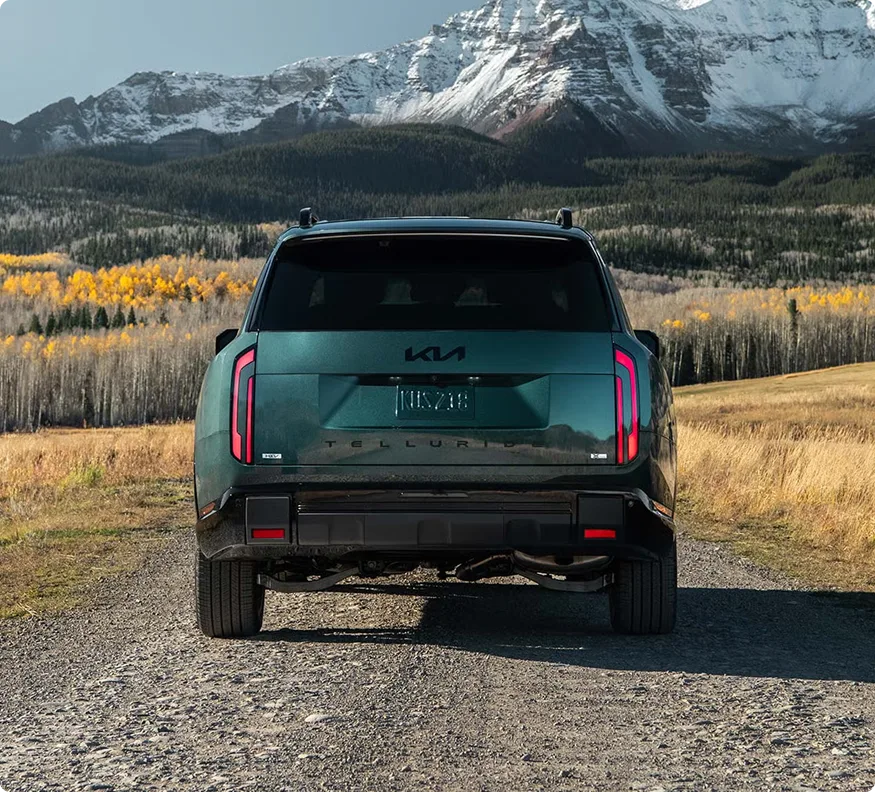 Dark green Telluride Hybrid seen from behind on a gravel road facing autumn hills