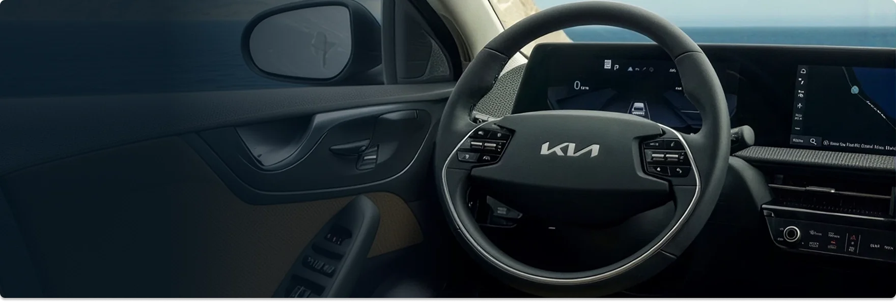 Kia steering wheel and digital instrument cluster seen from the driver's seat with the ocean through the windshield