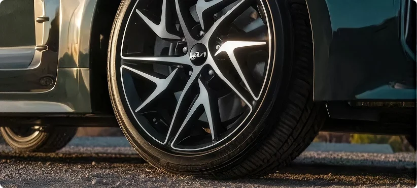 Close-up of a machined black-and-silver alloy wheel on a dark green Kia