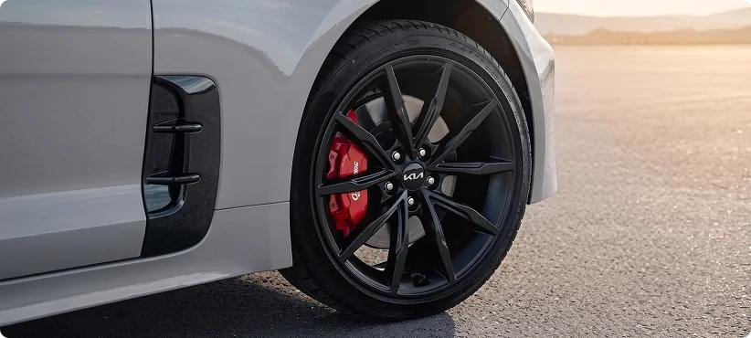 Close-up of the front wheel of a silver Kia Stinger with a black alloy rim and red brake caliper