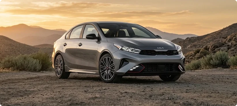 Silver Kia Forte GT parked on a desert road at sunset with mountains behind it