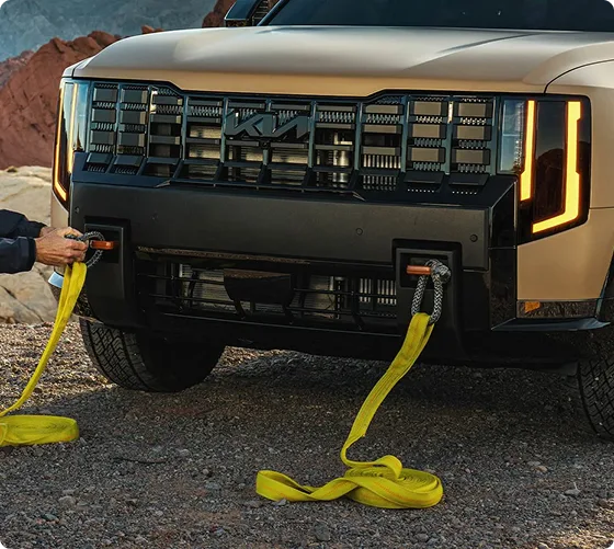 Person attaching yellow recovery straps to the front recovery hooks of a bronze Telluride