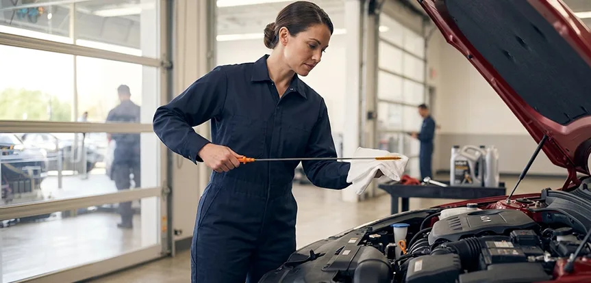 Technician checking the oil dipstick on a red Kia with the hood raised