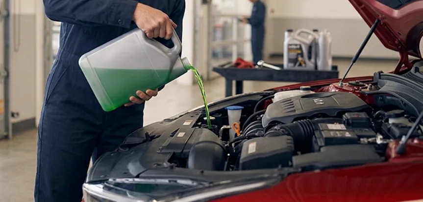 Technician pouring green coolant into the reservoir of a red Kia