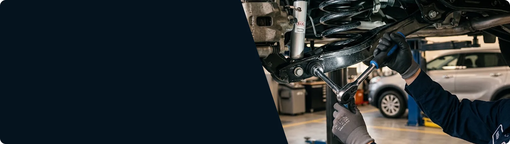 Kia technician working on a rear shock absorber and coil spring under a lifted vehicle