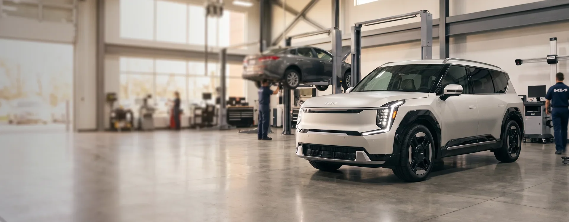 White Kia EV9 parked in the Briggs Kia of Topeka service shop while technicians work on other vehicles